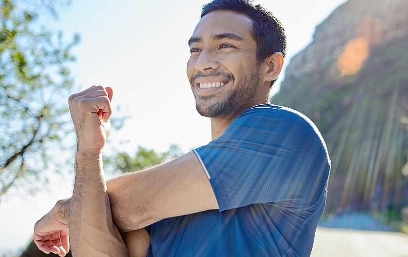 Smiling man stretching outdoors in bright sunlight.